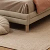 A close-up view of a bed frame with bedding and a rug. Produktbild-Vorschau