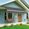 A gray awning is extended over the front porch of a blue house, providing shade for a wooden bench and the entrance. Produktbild-Vorschau