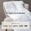 A white quilted blanket draped over a chair, with text overlay indicating design origin and publications it has been featured in. Produktbild-Vorschau