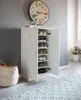 A white shoe cabinet filled with shoes, placed in a room with a large clock on the wall and a basket on the floor. Produktbild-Vorschau
