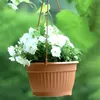 A hanging planter filled with white flowers against a blurred green background. Náhled obrázku produktu