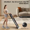 A woman is standing next to a folded treadmill in a living room. Náhled obrázku produktu