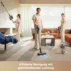 Three women are vacuuming a modern living room with a dog present. Voir les images du produit