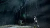 A person in a white suit stands in a dark, eerie forest with ancient statues and trees. Produktbild-Vorschau
