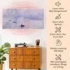 A painting is displayed on a wall above a wooden dresser. Text and icons describing product features are on the right side of the image. Produktbild-Vorschau