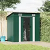 A green metal garden shed with its doors open, showing gardening tools inside, set in a backyard with a wooden fence and green foliage.