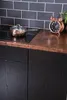 A close-up shot of a kitchen counter with black wooden cabinets, a copper countertop, and a tiled backsplash. Produktbild-Vorschau