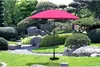 A pink patio umbrella stands in a beautifully landscaped garden with rocks and manicured bushes. Produktbild-Vorschau