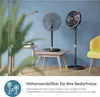Two black pedestal fans are shown in a room setting with a blue wall, a yellow chair, and a small wooden table with books. Anteprima dell’immagine prodotto