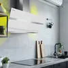 A modern kitchen scene featuring a white glass range hood above a stovetop, with a sink and cutting boards in the background. Produktbild-Vorschau