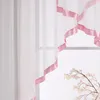 A close-up view of a sheer white curtain with a pink satin ribbon trim, hanging in front of a window. Produktbild-Vorschau