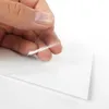 A hand is peeling a clear protective film off a white sheet, likely a sticker or adhesive material. Produktbild-Vorschau