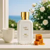A perfume bottle is displayed on a windowsill with a cup of tea and caramel candies, with a view of the ocean and flowers in the background. Anteprima dell’immagine prodotto