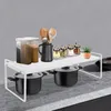 A white metal shelf unit is placed on a countertop, holding kitchen items like spice jars, utensils, and pots. Náhled obrázku produktu