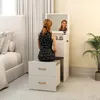 A woman sits at a vanity table in a bedroom setting. Produktbild-Vorschau