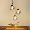 Three pendant lights with geometric metal cages and wooden accents hang above a wooden table with decorative items. Voir les images du produit