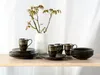 A set of stoneware mugs and plates with a decorative pattern, arranged on a wooden surface with a vase of branches in the background. Náhľad obrázku produktu
