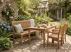 Massive Teakholzbank Kingsbury 180 cm mit Rückenlehne, Kissen und Tablett in Gartenumgebung neben Holztisch und Stühlen. Produktbild-Vorschau