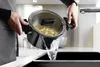A person is draining water from a pot of pasta into a sink. Produktbild-Vorschau