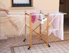 A person's hand is adjusting a wooden and white clothes drying rack with laundry on it, outdoors on a tiled patio. Anteprima dell’immagine prodotto