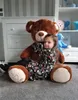 A young girl hugging a large teddy bear in a room with a dresser and shelves. Podgląd zdjęcia produktu