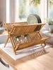 A wooden dish drying rack filled with plates and glasses on a kitchen counter by a window. Produktbild-Vorschau