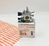 A carburetor is shown on top of its packaging, with some protective material in the foreground. Produktbild-Vorschau