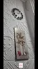 A wall decorated with white textured panels, featuring a clock and a framed picture of a vase with flowers and two red hearts. Produktbild-Vorschau