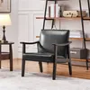 A black armchair with wooden armrests and legs is placed on a rug in a room with a bookshelf in the background. Produktbild-Vorschau