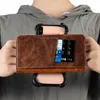A person is holding a brown leather wallet-style phone case with credit cards inserted. Produktbild-Vorschau