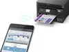 A smartphone is shown displaying the Epson Smart Panel app, with wireless signals connecting it to an Epson EcoTank L6270 printer that is printing a document. Podgląd zdjęcia produktu