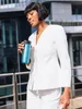 A woman in a white suit holding a blue travel mug outside a modern building. Produktbild-Vorschau