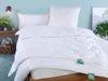 A neatly made bed with white bedding, pillows, and a duvet, set against a light blue wall. Decorative elements like a plant and a basket of magazines add to the scene. Produktbild-Vorschau
