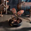 A steampunk-style mechanical rhinoceros beetle model on a dark circular base, set against a background of industrial pipes and tanks. Náhľad obrázku produktu