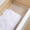 A white folded shirt lies inside a wooden drawer lined with a beige mat. Voir les images du produit