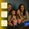 A family is watching a movie projected by a mini projector, with popcorn. Voir les images du produit
