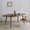 An oval dining table with a chair and decorative items in a room with a grid-patterned wall. Produktbild-Vorschau