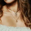 Close-up of a woman wearing layered gold necklaces with charms. Produktbild-Vorschau