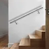 A stainless steel handrail mounted on a white wall next to a wooden staircase. Náhled obrázku produktu