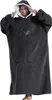 A woman wearing a dark gray oversized hoodie blanket with a white interior lining and a pocket with an apple design. Produktbild-Vorschau