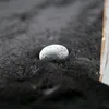 A close-up of a small, gray, textured stone resting on a dark, fluffy, carpet-like surface. The lighting is soft, creating a shallow depth of field. Anteprima dell’immagine prodotto