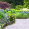 A garden path bordered by wooden palisades and filled with various colorful flowers and lush greenery. Náhled obrázku produktu