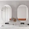 A modern bathroom with two oval mirrors above a marble countertop with sinks and faucets. Podgląd zdjęcia produktu