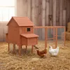 A wooden chicken coop with an attached run, set in a straw-covered outdoor area with hay bales and a shovel in the background. Náhled obrázku produktu