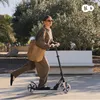 A woman riding a scooter in an outdoor park setting. Produktbild-Vorschau