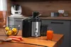 A kitchen counter with a juicer, carrots, lemons, and a glass of juice. Produktbild-Vorschau
