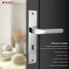 A close-up of a chrome door handle on a dark door, with a blurred background of a room interior. Produktbild-Vorschau