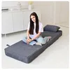 A young woman is sitting cross-legged on a folded mattress in a room with a white cabinet in the background. Voir les images du produit