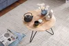 A round wooden coffee table with a black teapot, a small cup, and decorative items on a rug next to a blue sofa. Náhled obrázku produktu