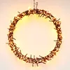 A circular wreath made of brown twigs and illuminated by warm white LED lights, hanging against a light gray background. Produktbild-Vorschau
